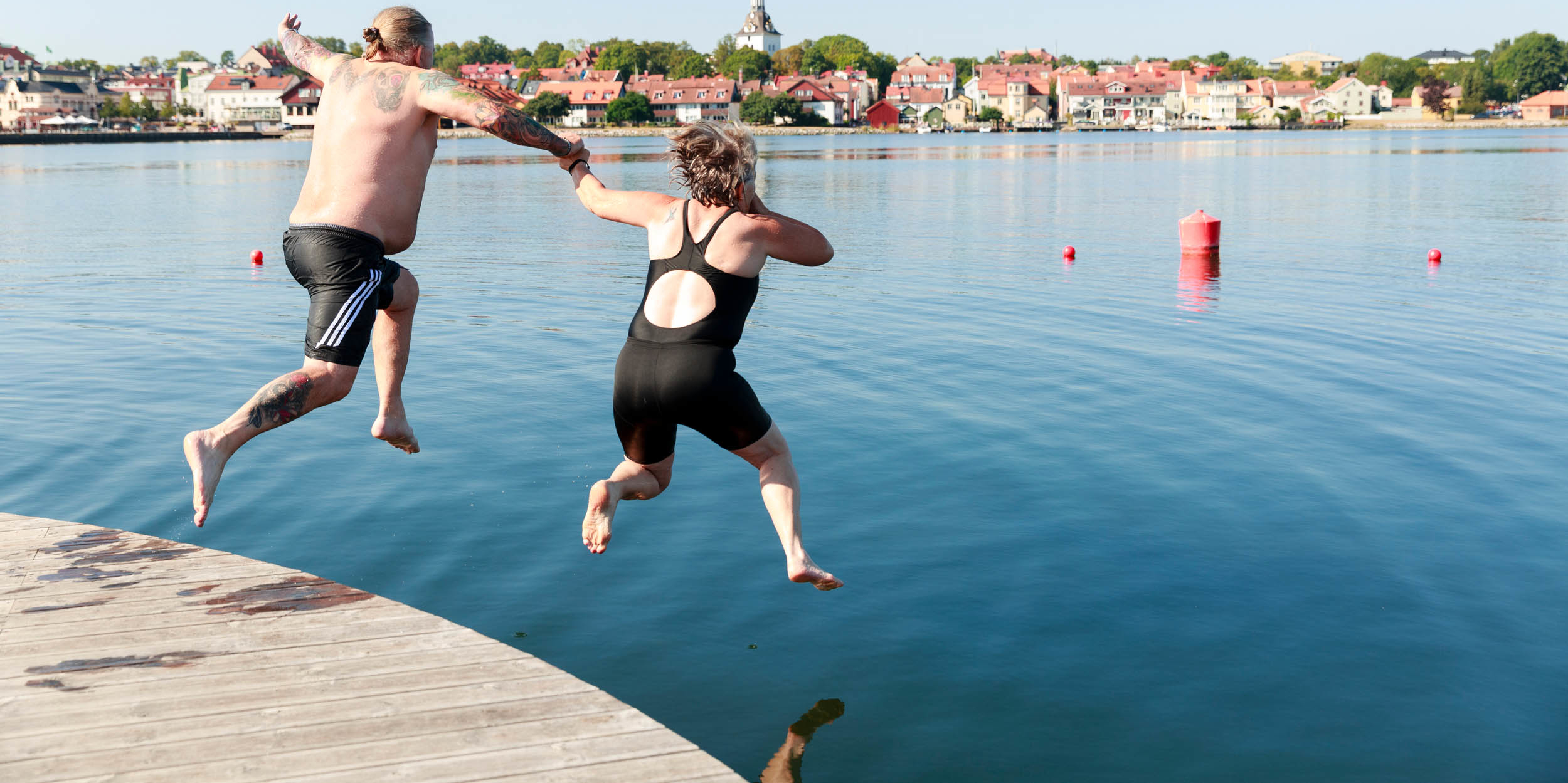 Badande par som hoppar från kajkanten.