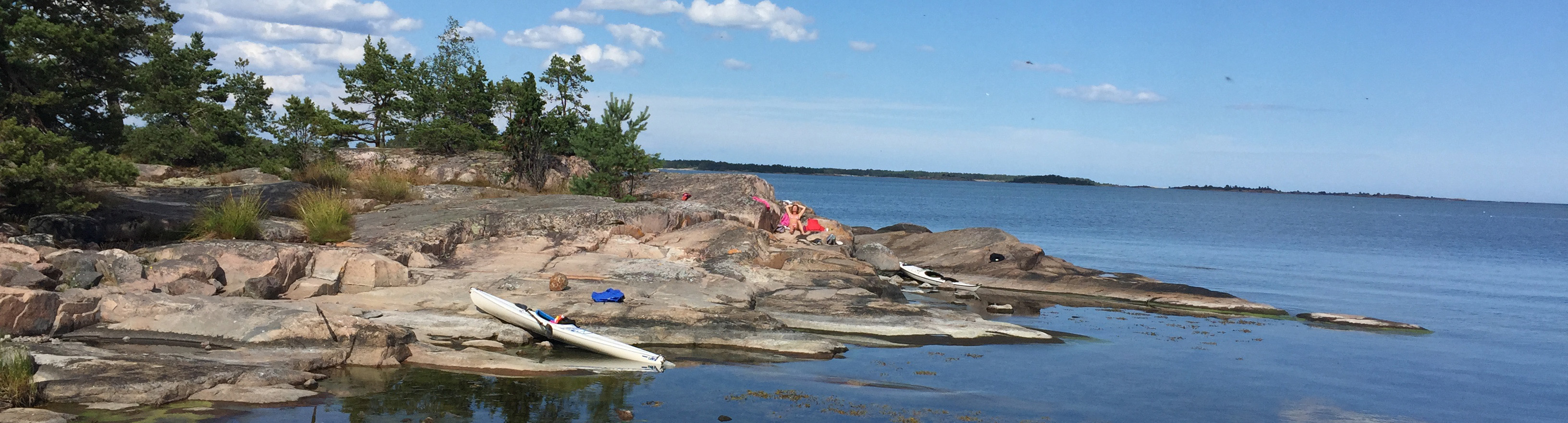 En människa ligger och solar på en klippa i skärgården.